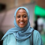 Portrait of a smiling woman in a blue hijab and dress, outdoors.